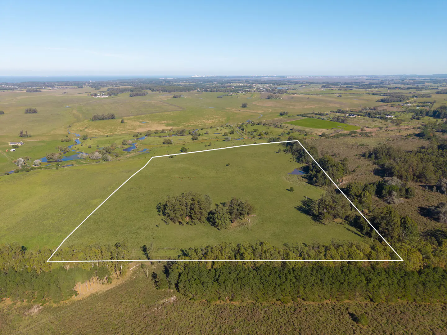 Aerial view of a large, green grassy plot of land outlined in white, surrounded by trees and open countryside.