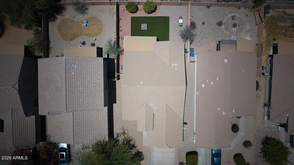 Aerial view of a suburban home with a tan tile roof, a small green lawn, and desert landscaping in the backyard.