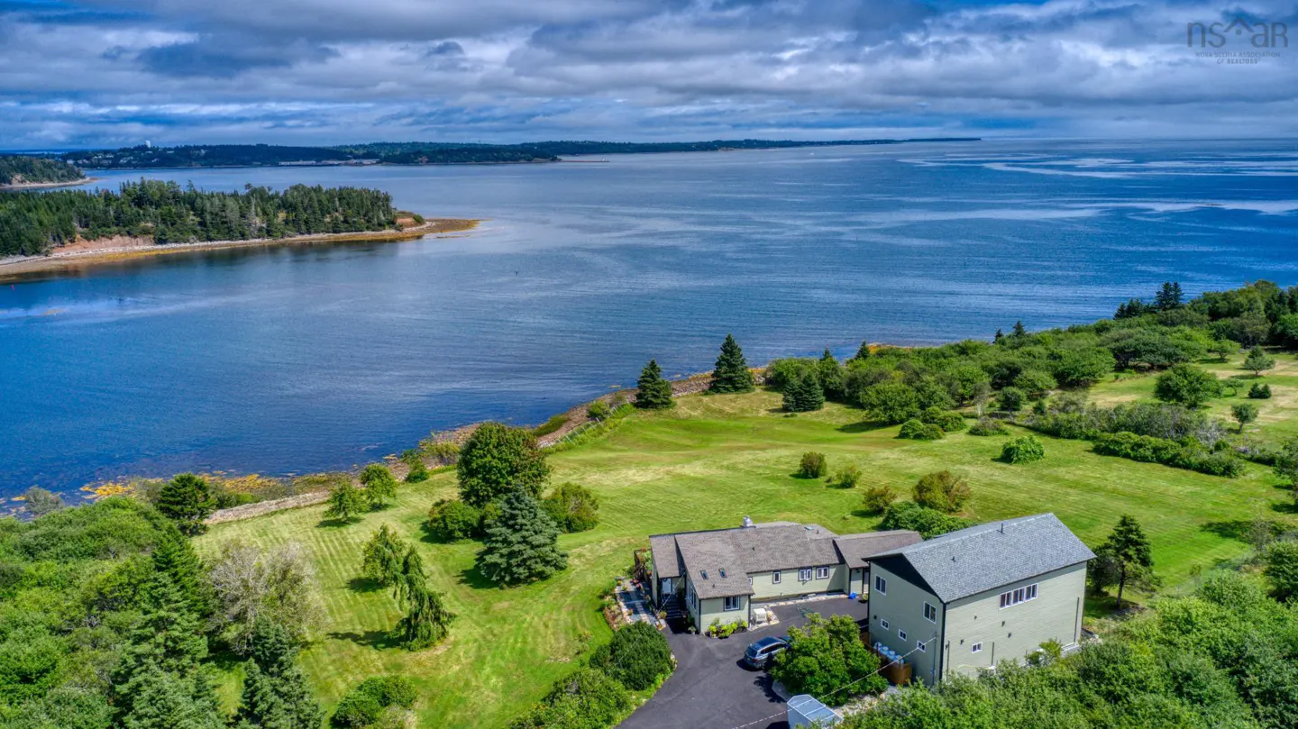 Aerial view of a light green house on a grassy lawn near a blue ocean under a cloudy sky.