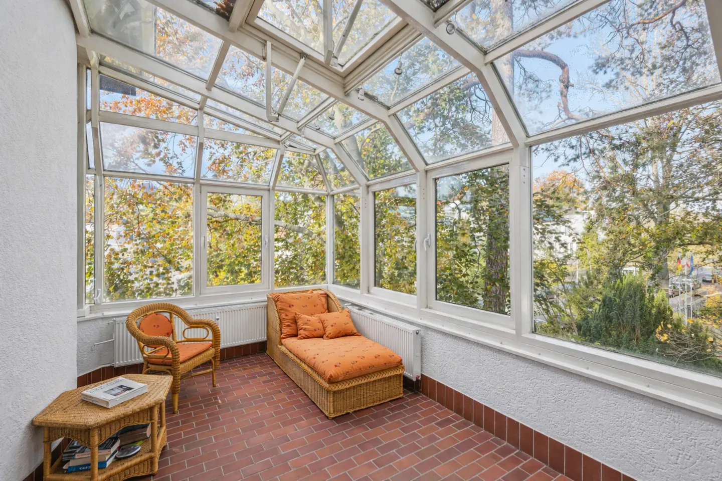 Sunroom with brick floor, white walls, and glass ceiling. Wicker furniture includes a chair, chaise lounge, and side table.