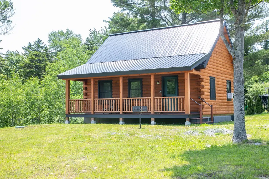 Exterior view of a log cabin with a metal roof, a porch, and a green lawn.