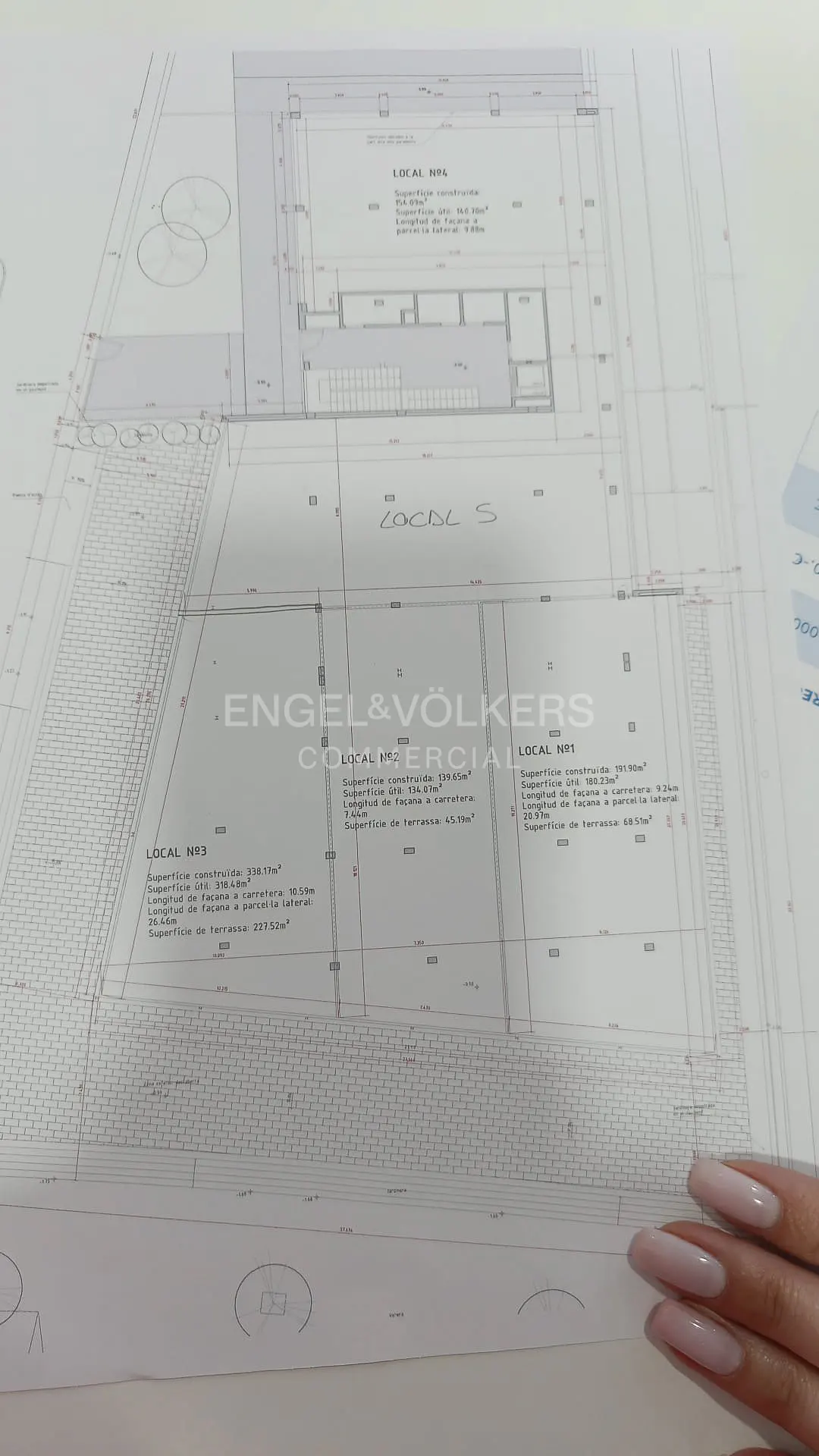 Blueprint of commercial spaces by Engel & Völkers, with measurements and layout details. A hand with long nails is visible.