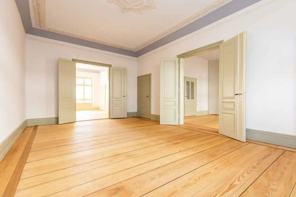 Empty room with light wood floors, white walls, decorative ceiling molding, and open double doors leading to other rooms.