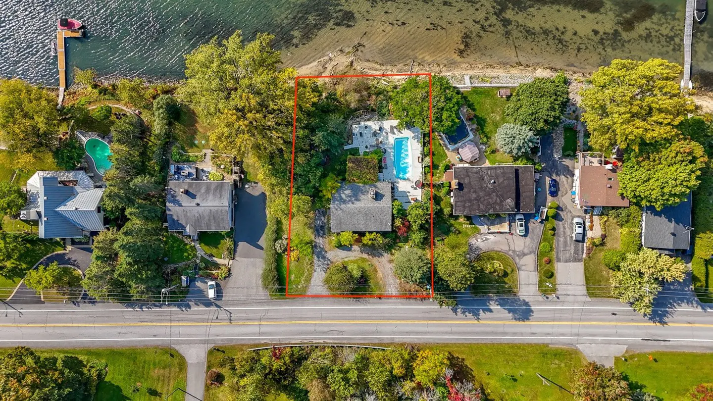 Aerial view of a property outlined in red, featuring a house, pool, and lake access.