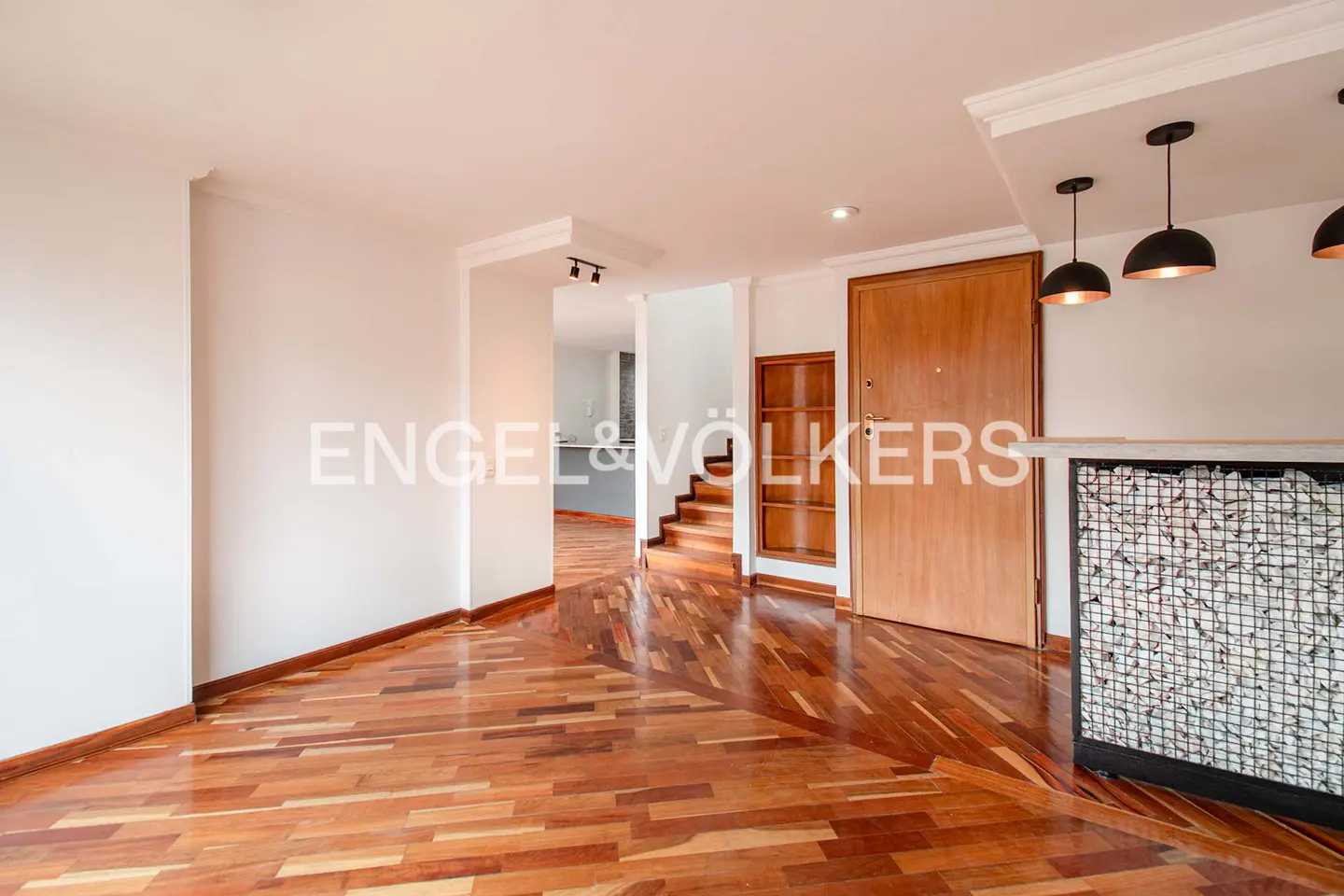 Modern interior with hardwood floors, a wooden door, a stone-filled bar counter, and stairs leading to a kitchen area.