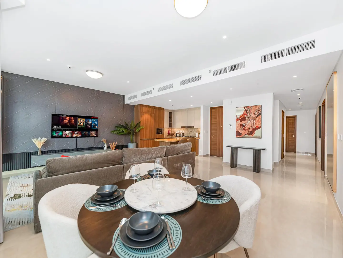 Bright, modern apartment interior with a round dining table set for four, a gray sofa, and a TV on a gray accent wall.