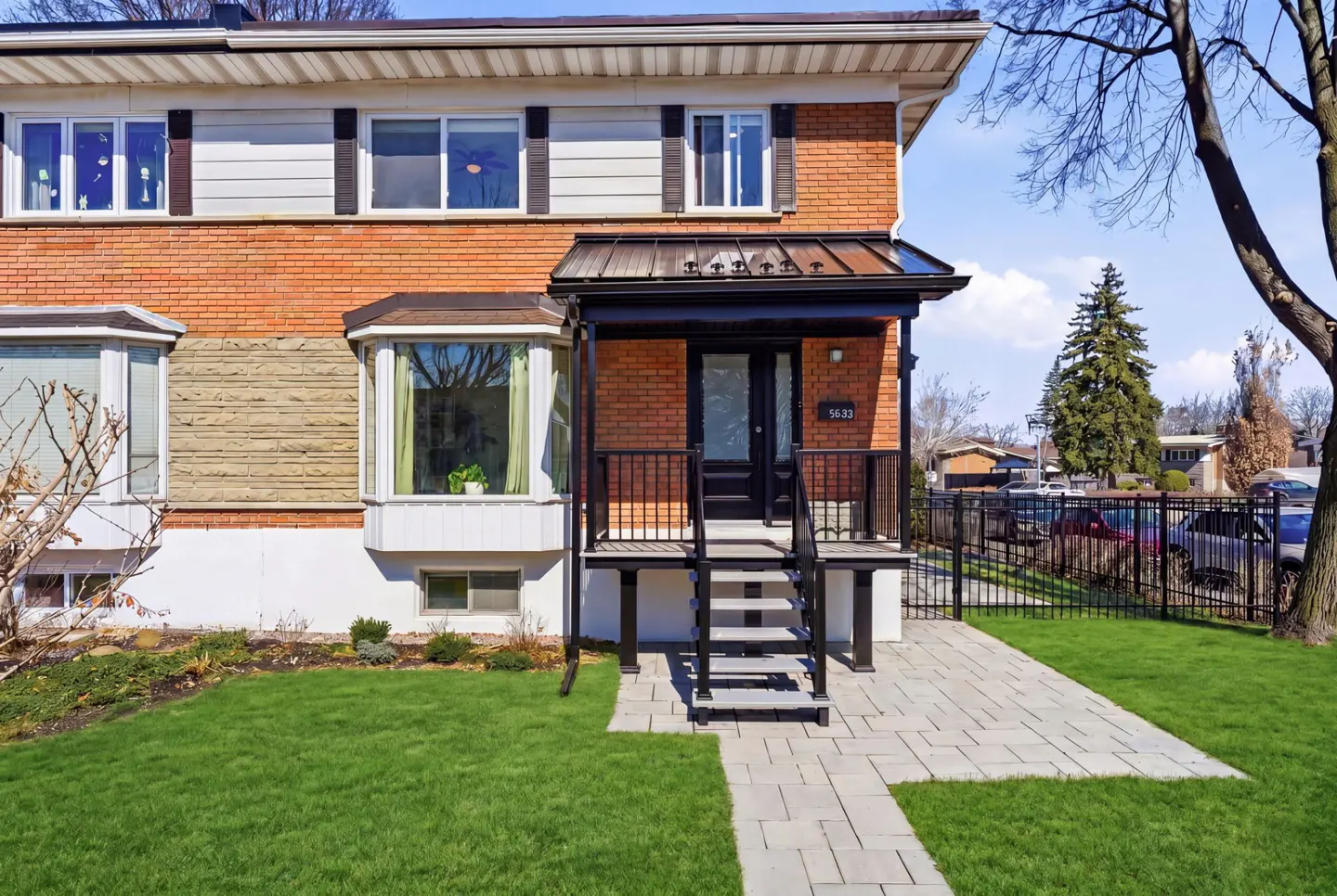 Exterior of a two-story brick house with a black door, porch, and a green lawn.
