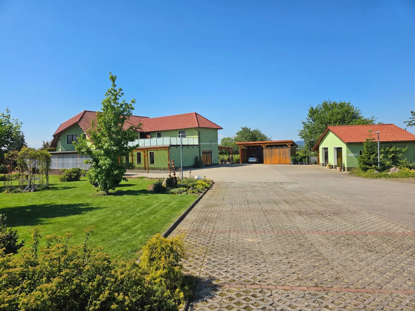 Exterior view of a green house with a red tile roof, a lawn, and a stone parking area under a clear blue sky.
