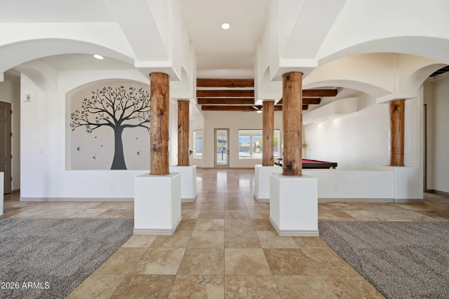 Open floor plan with tile floors, rustic wooden pillars, arched ceilings, and a wall mural of a tree in a bright room.