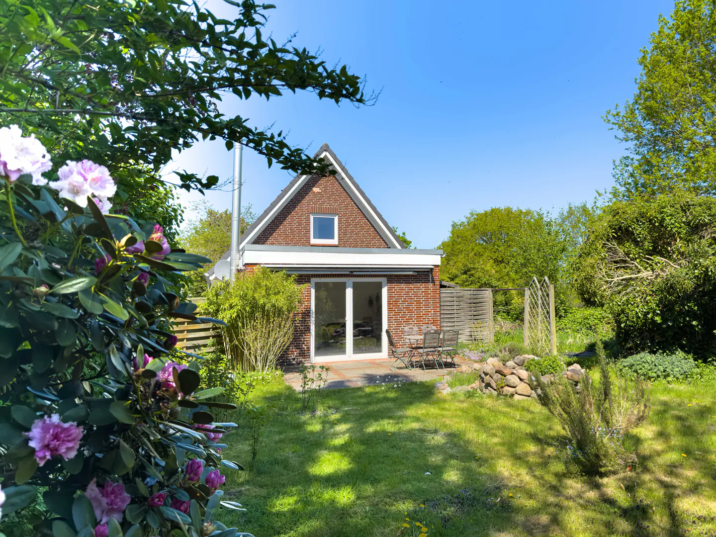 A red brick house with a green lawn and trees under a blue sky.