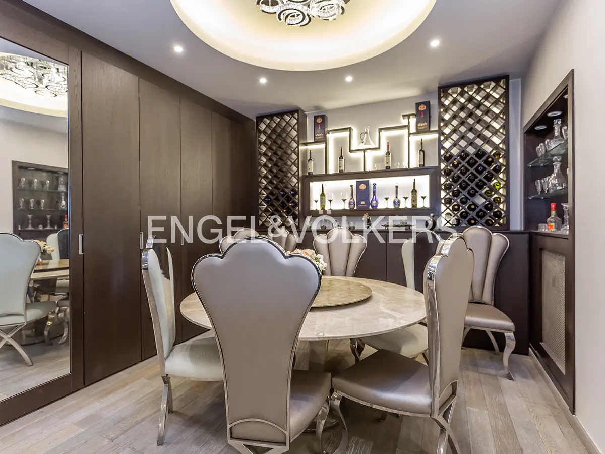 Dining room with a round table, upholstered chairs, and a built-in wine rack with bottles.