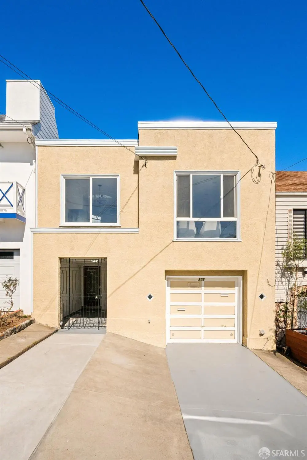 Exterior of a two-story beige stucco home with a white garage door, a front entrance gate, and a concrete driveway.