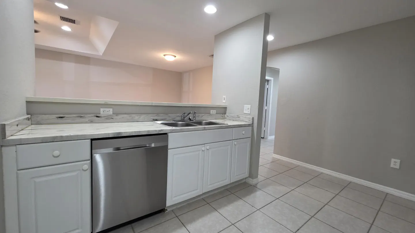 A kitchen with white cabinets, stainless steel dishwasher, marble countertops, and tile flooring.