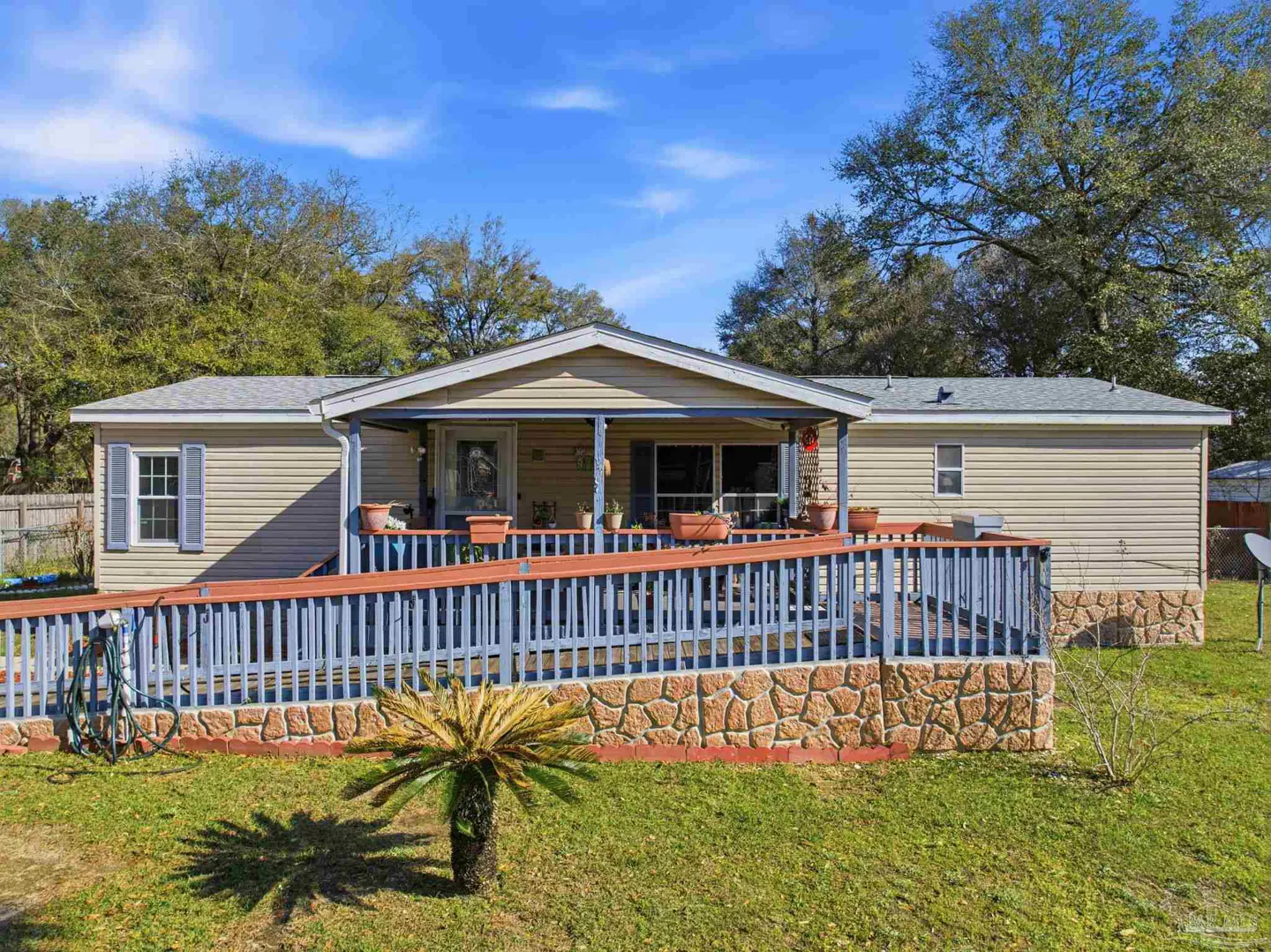 Tan single-story home with a blue-railed ramp leading to a covered porch. A small palm tree sits in the green lawn.