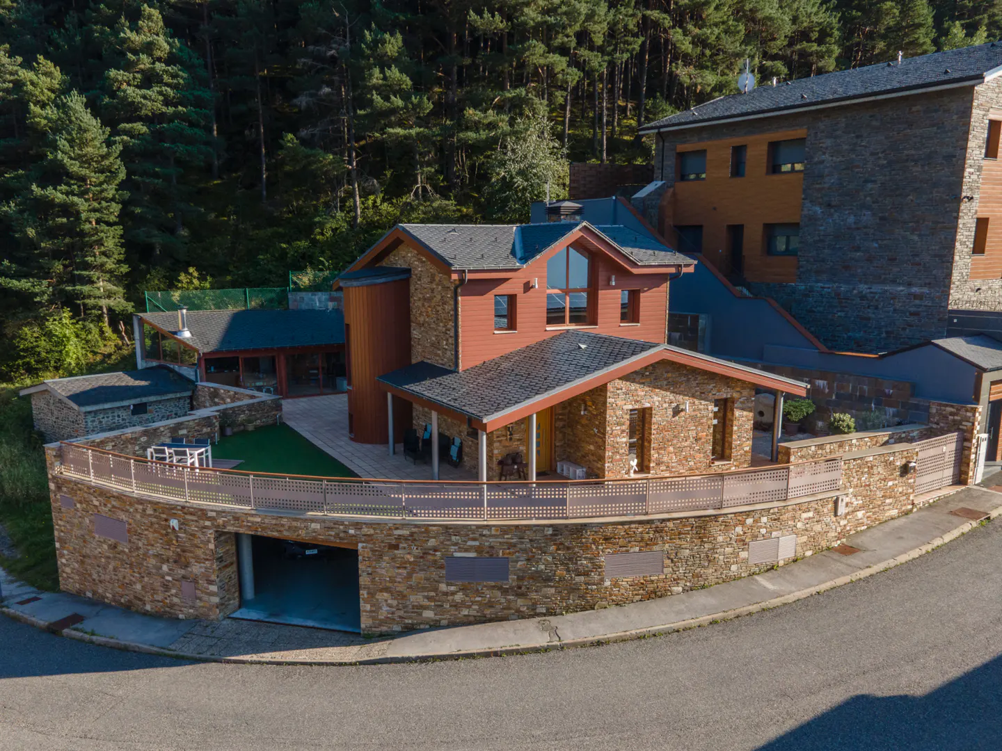A modern two-story house with a stone facade and a dark gray roof, surrounded by green trees.