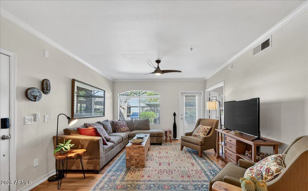 Living room with brown sectional sofa, patterned rug, TV, and two armchairs. A ceiling fan is visible.