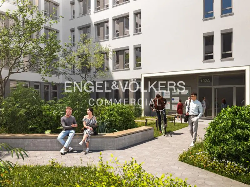 Exterior view of a white commercial building with people walking and sitting outside. The Engel & Volkers logo is visible.