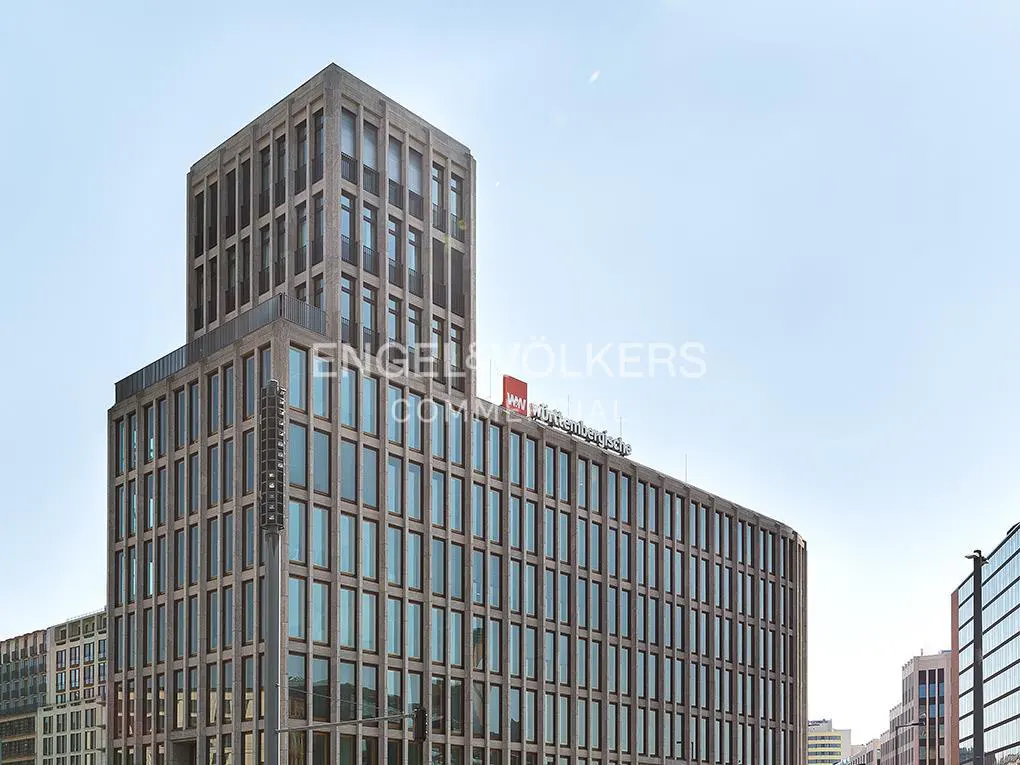 Modern brown office building with a grid-like facade and a tall tower section against a clear sky.