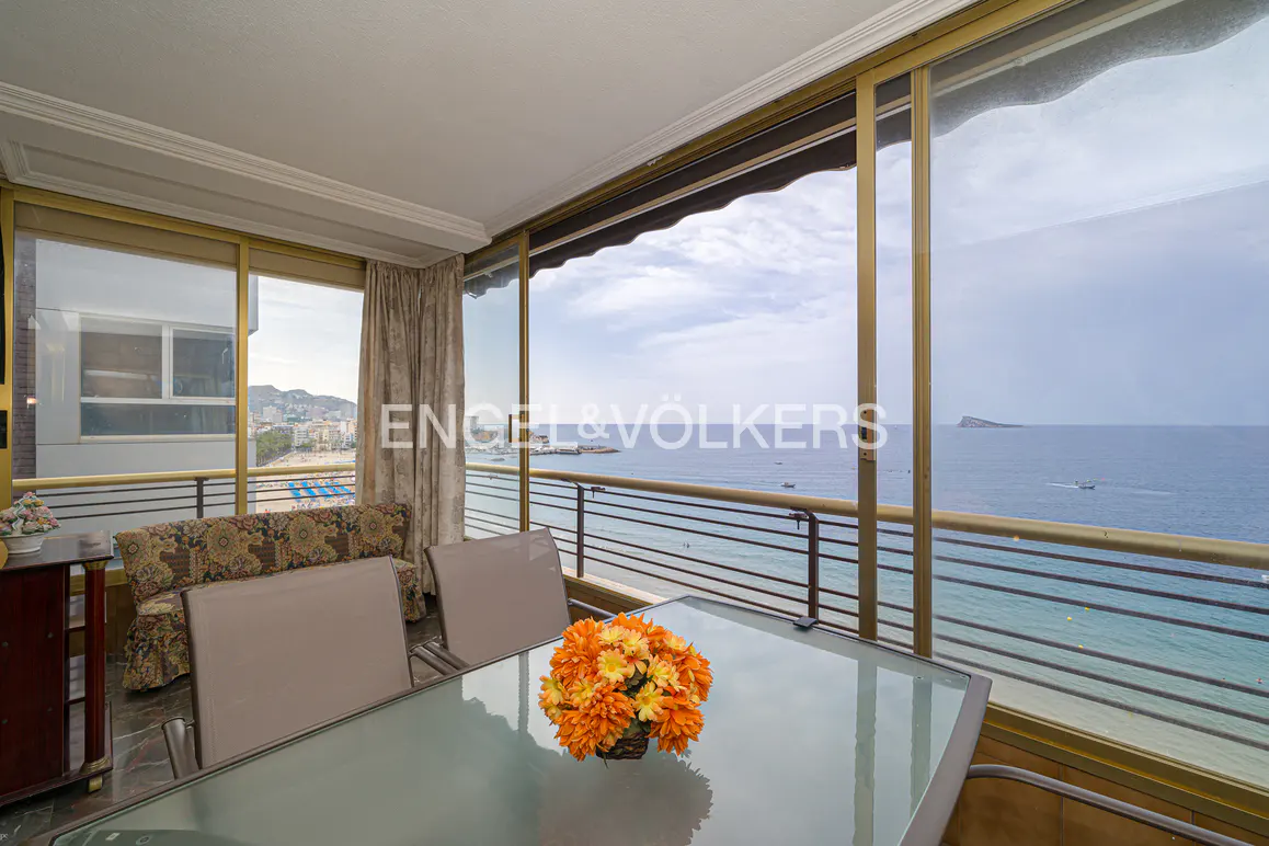Balcony view of ocean. Table with orange flowers, chairs, and sofa. Engel & Völkers logo on window.