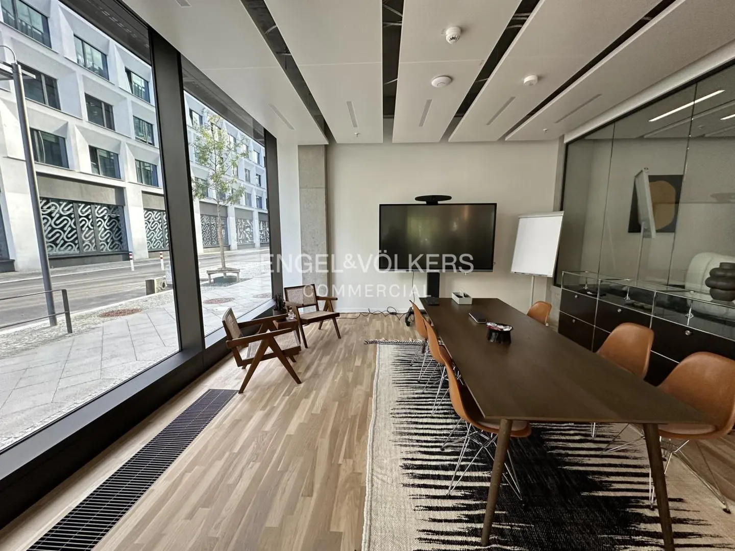 A modern office space with a long conference table, brown chairs, and a large window overlooking a city street.