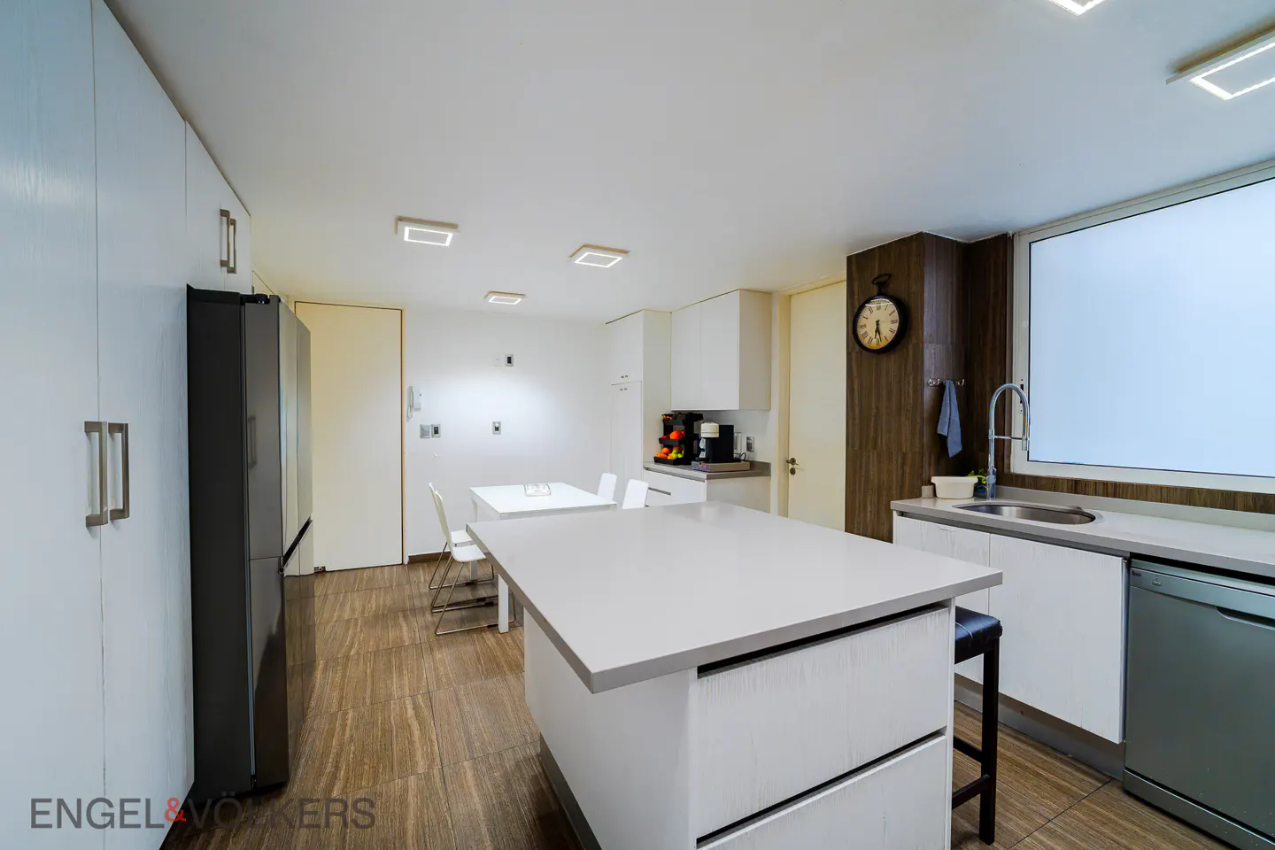 Modern kitchen with white cabinets, a central island, stainless steel appliances, and a dining area on wood-look tile floors.