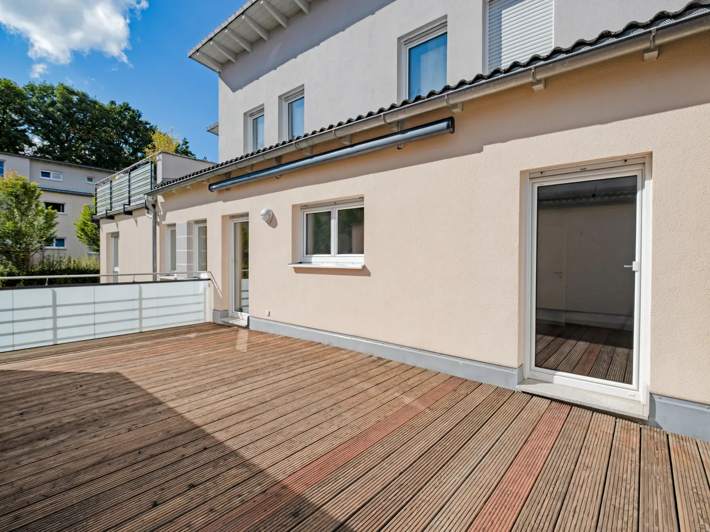 Exterior view of a two-story house with a wooden deck, white trim, and a beige exterior wall. Windows and doors are visible.
