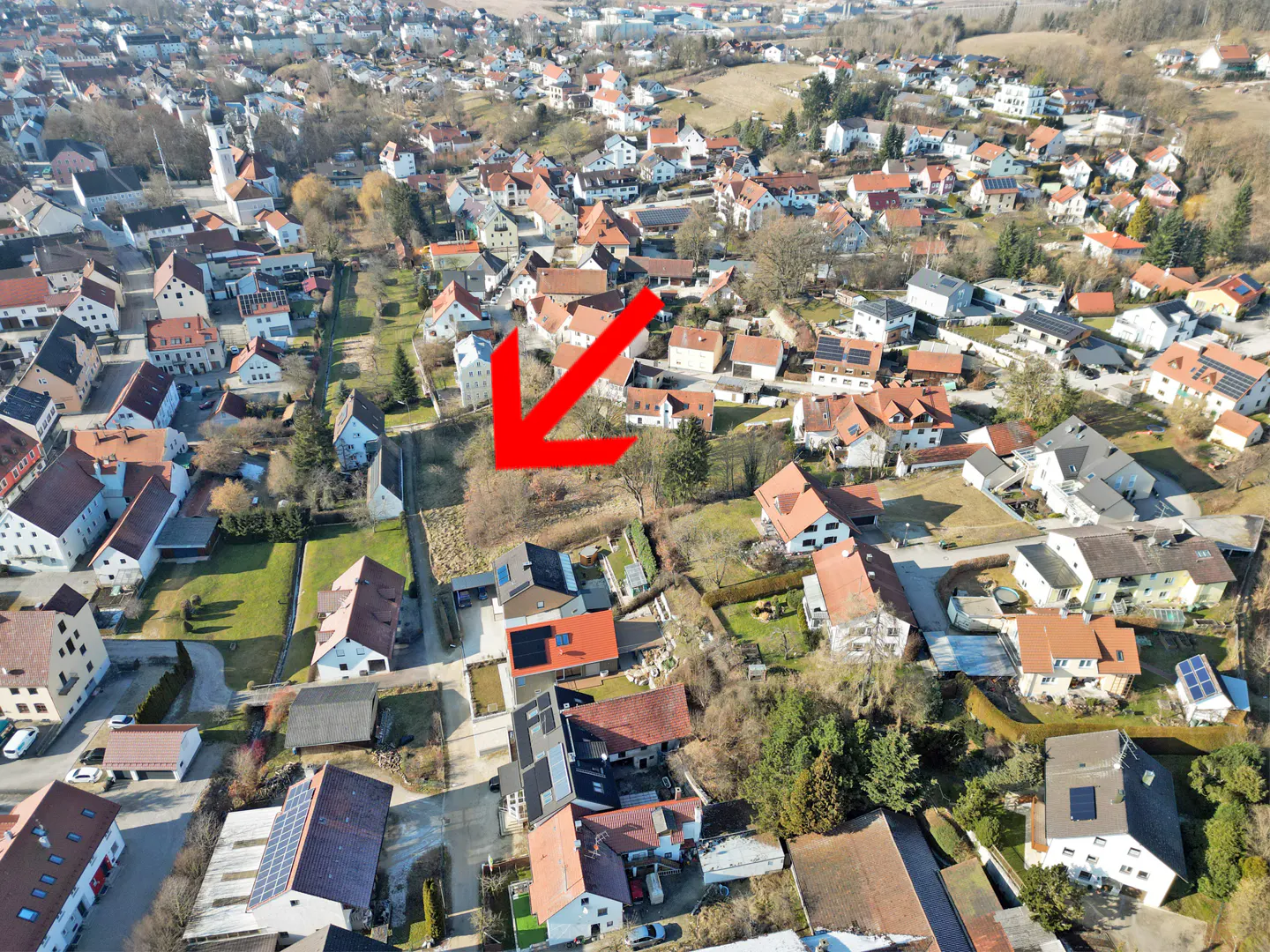 Aerial view of a village with houses, trees, and a red arrow pointing to a property.