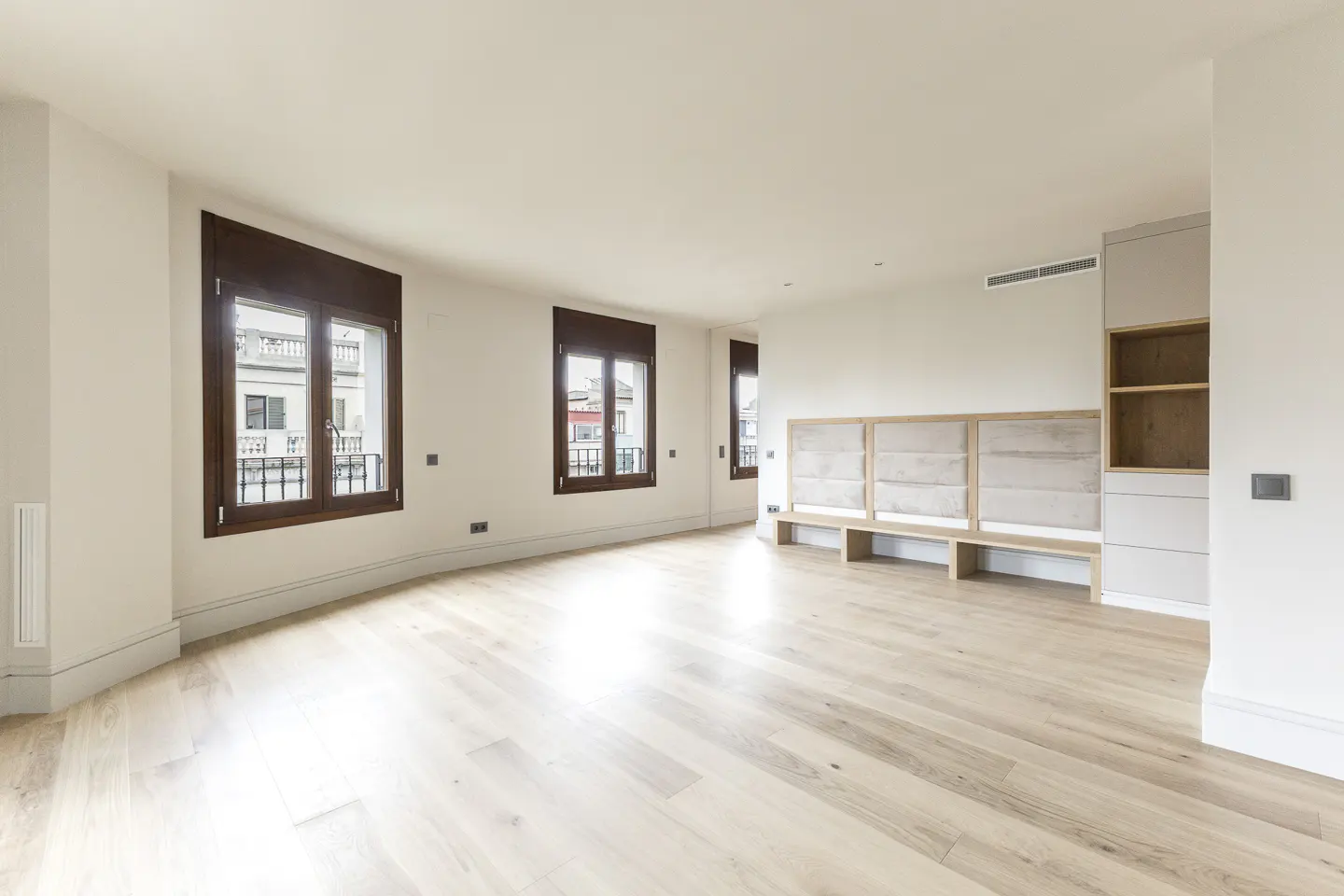 Bright, minimalist living room with light wood floors, white walls, dark-framed windows, and built-in bench seating.
