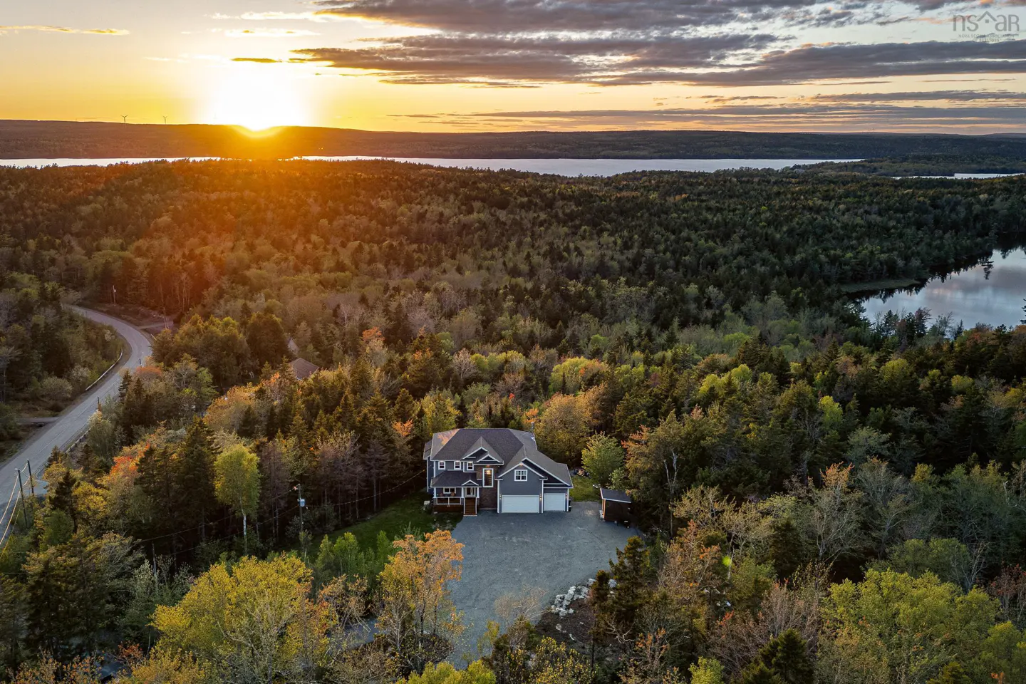 Aerial view of a gray two-story house surrounded by a forest at sunset.