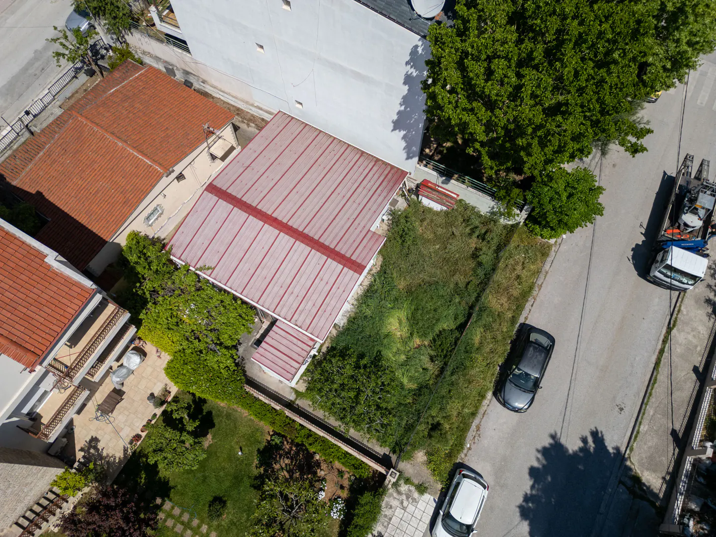 Aerial view of a house with a red roof, overgrown yard, and cars parked on the street.