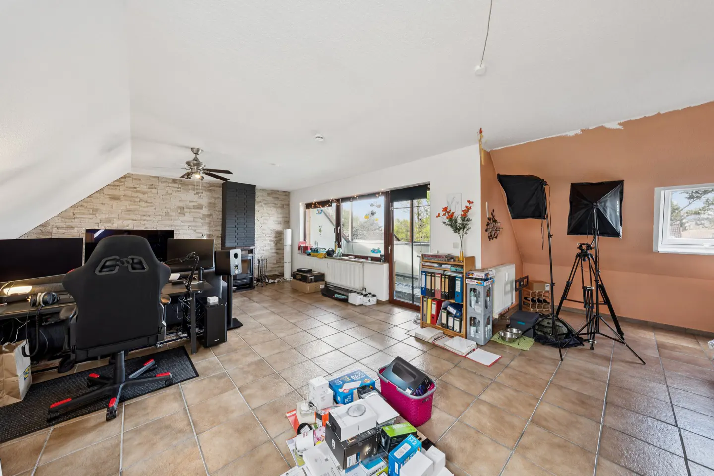 Attic home office with tiled floor, gaming chair, desk, shelving, and photography lighting equipment.
