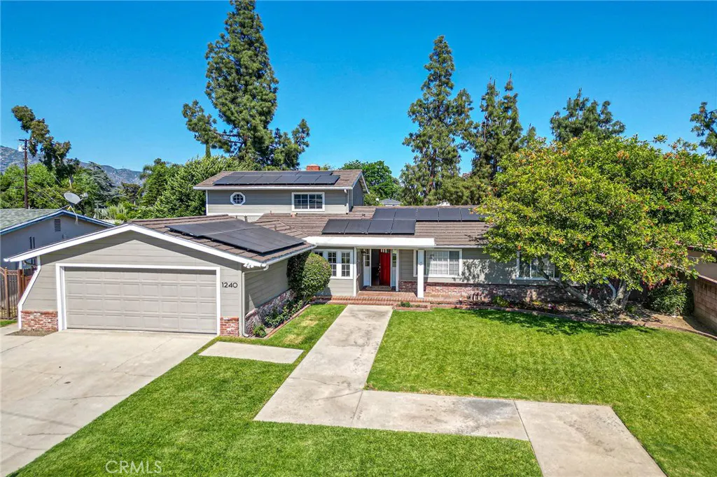 Two-story gray house with a red door, solar panels, and a green lawn on a sunny day.