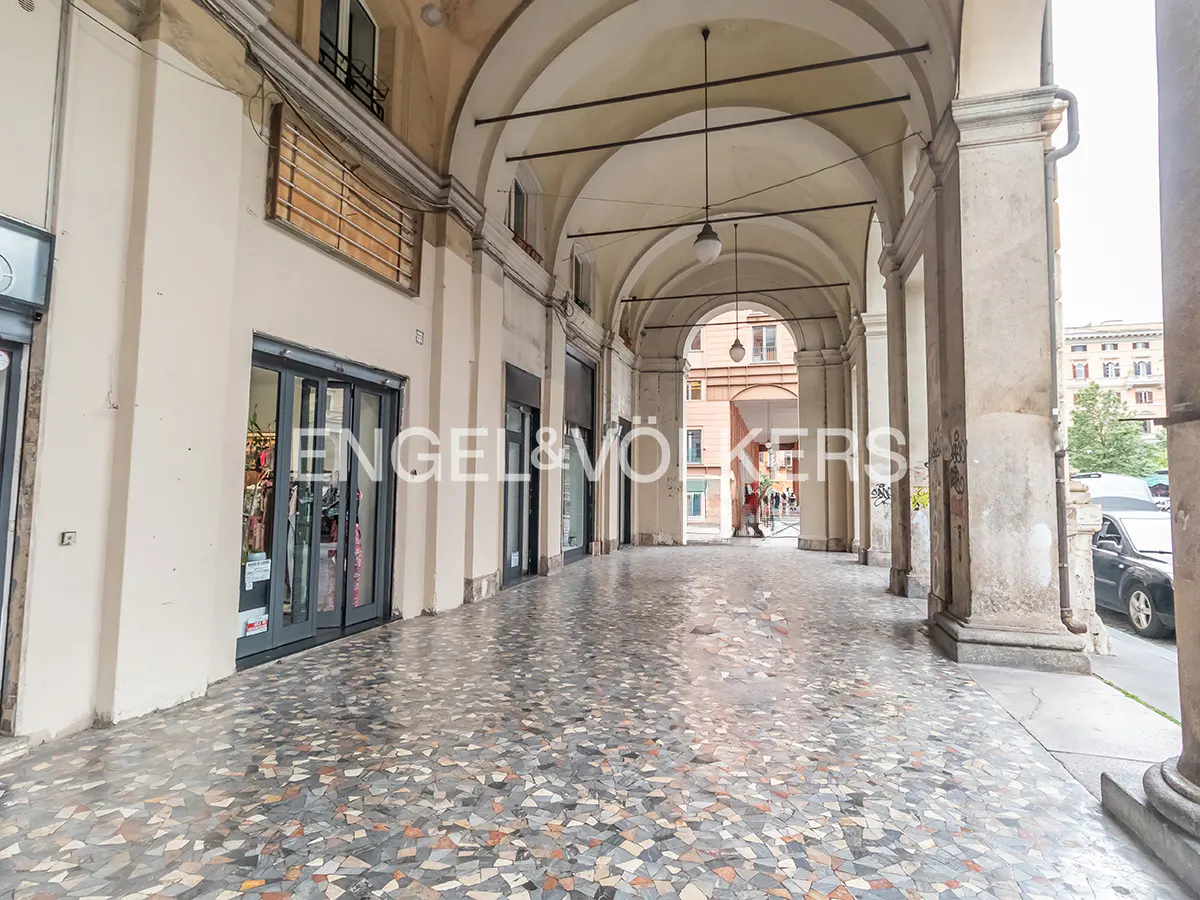 Covered walkway with arched ceilings and mosaic tile floor. Shops line the left side, and columns support the arches on the right.