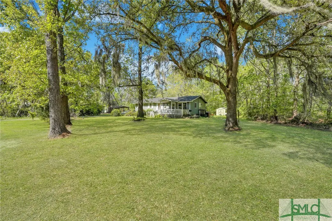 A green house with a porch sits on a large green lawn with trees and Spanish moss.