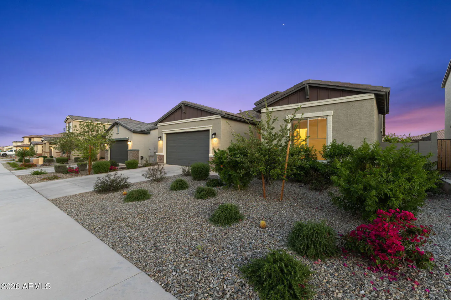 A row of single-story homes with gray garages and rock landscaping under a blue and pink twilight sky.