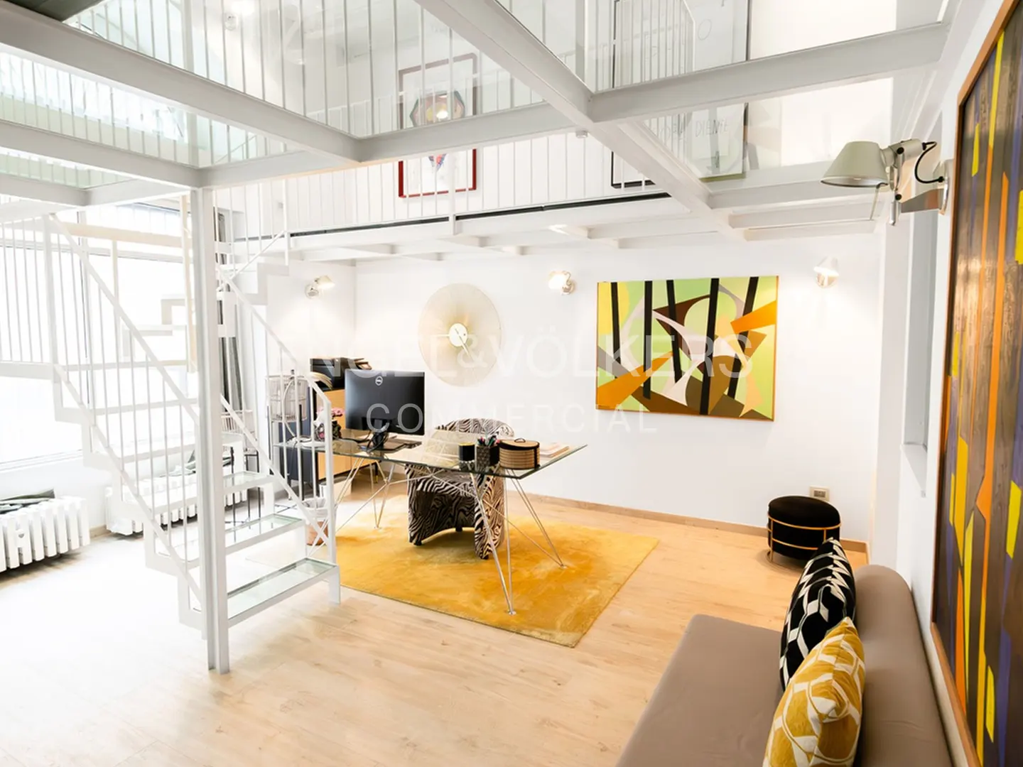 Bright, modern office space with white spiral staircase, glass desk, and yellow rug. Abstract art adorns the white walls.