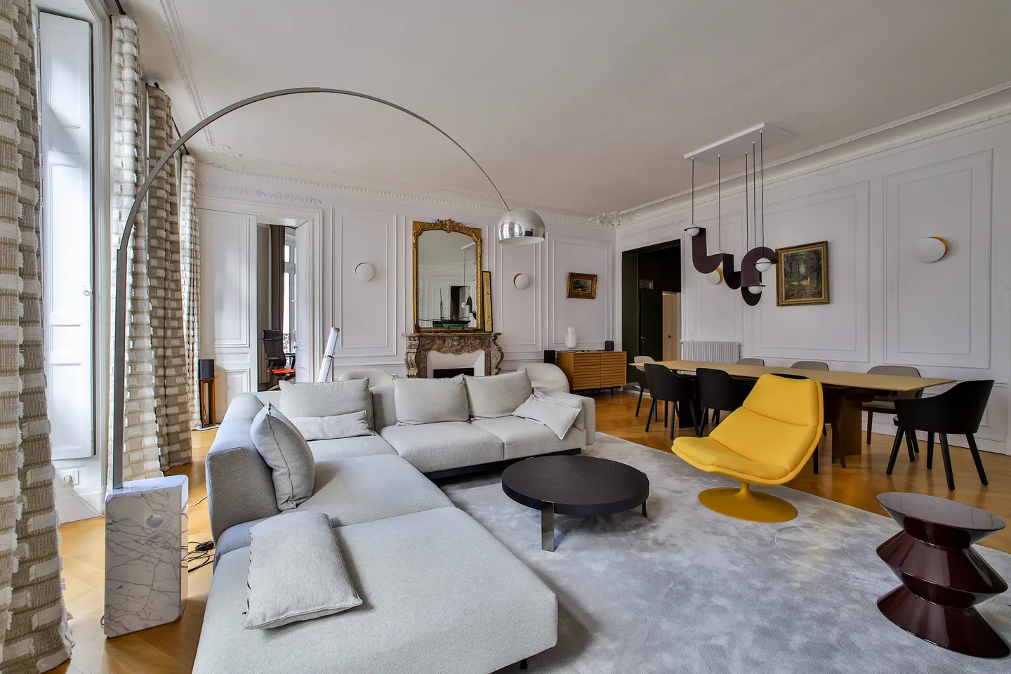 Modern living room with a large grey sectional, a bright yellow armchair, a round coffee table, and a tall arched lamp.