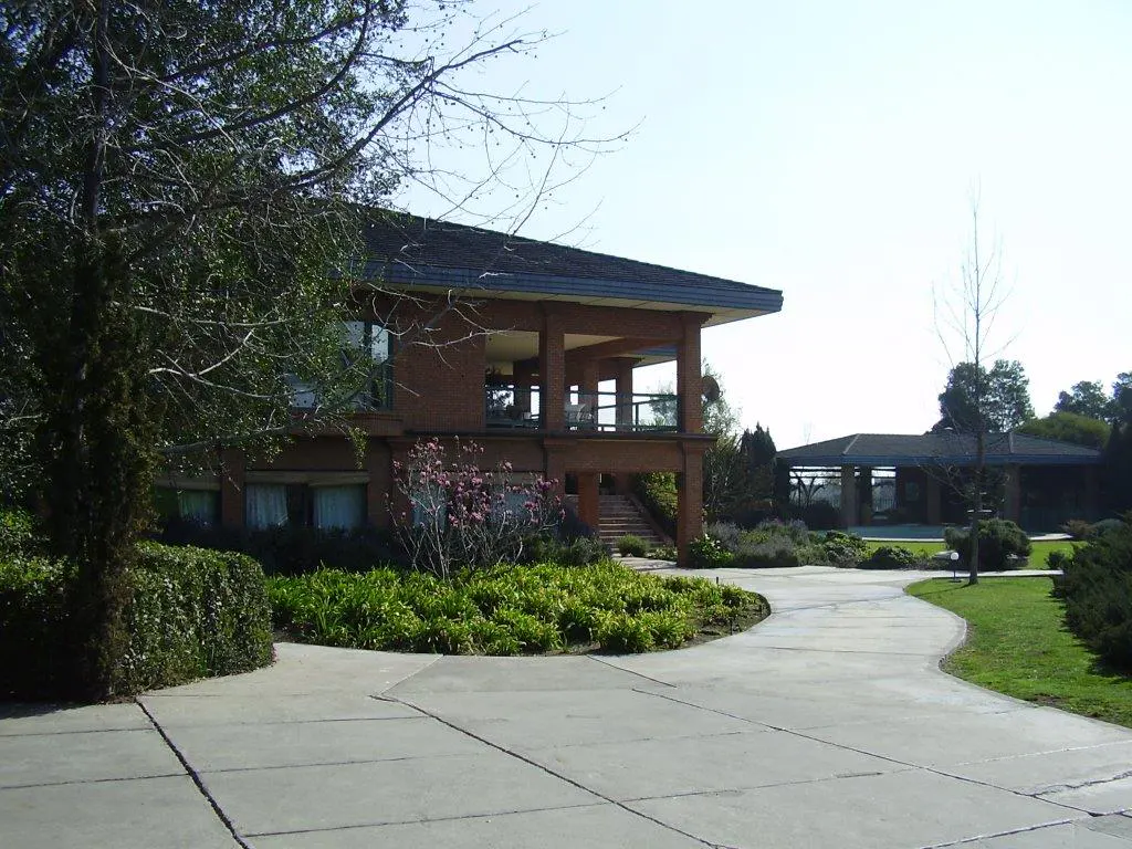 Two-story brick house with a covered porch, surrounded by green landscaping and a winding concrete driveway.