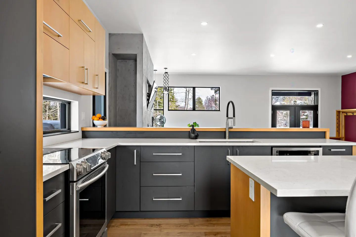 Modern kitchen with gray cabinets, stainless steel appliances, and a white countertop. Light wood cabinets above and a view of trees through the window.