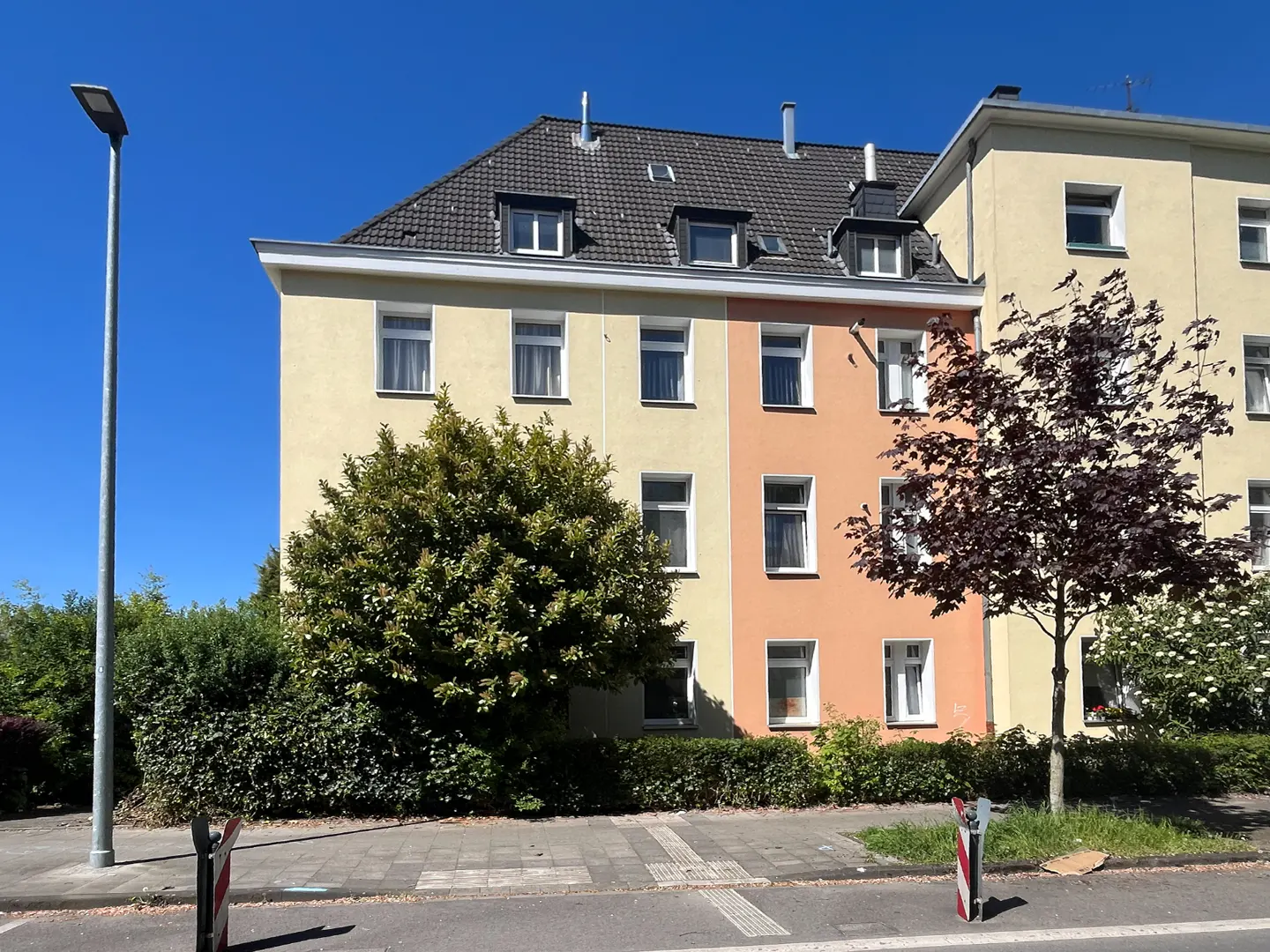Exterior view of a three-story apartment building with yellow and peach facade, dark roof, and green trees.