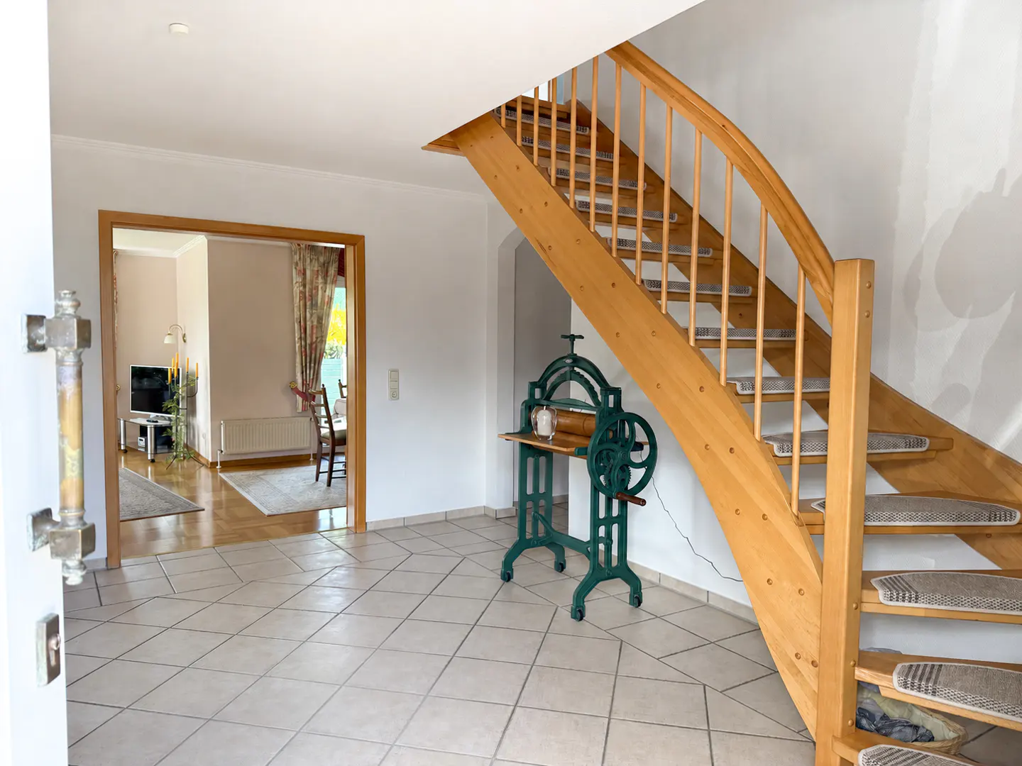 Foyer with a wooden staircase, a green antique mangle, and a view into a living room with a TV and dining area.