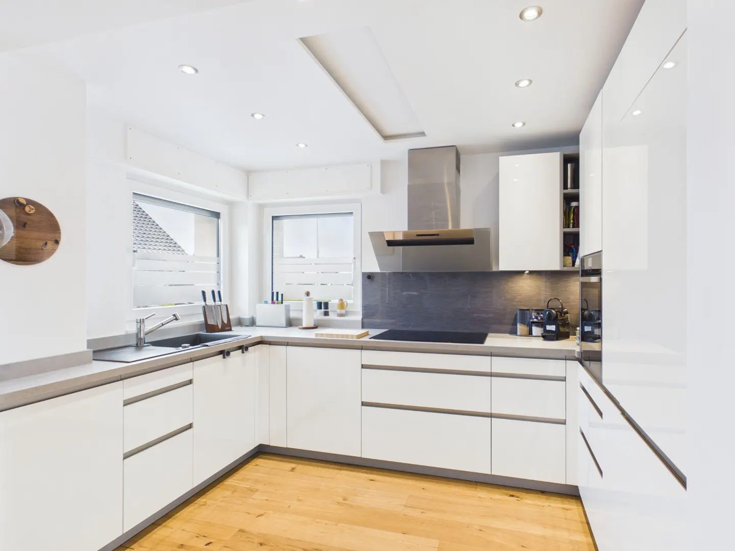 Modern kitchen with white cabinets, grey countertops, stainless steel appliances, and light wood flooring.