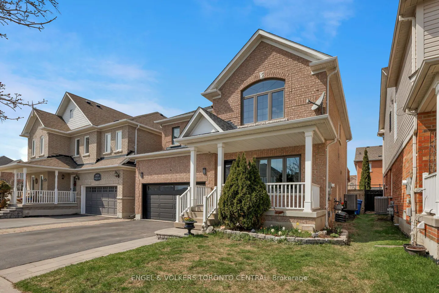 Two-story brick house with a front porch, white railings, and a dark gray garage door under a blue sky.