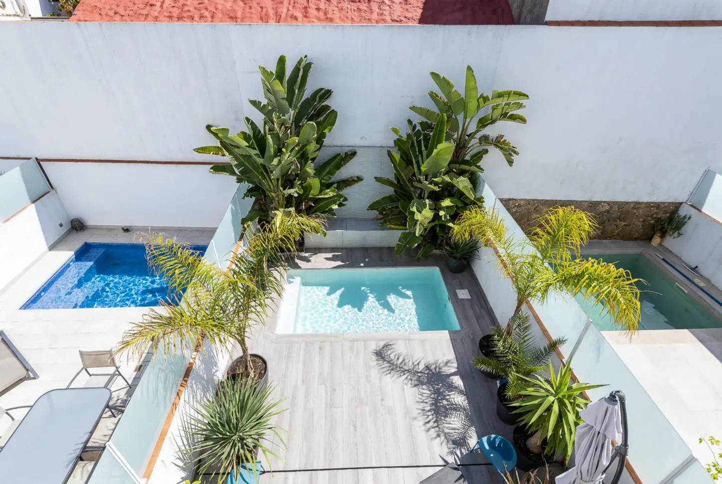 Aerial view of a courtyard with three small pools, surrounded by white walls and lush green plants.
