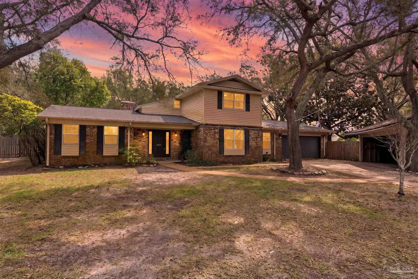 Two-story brick and tan siding house with black shutters and a pink and purple sunset.