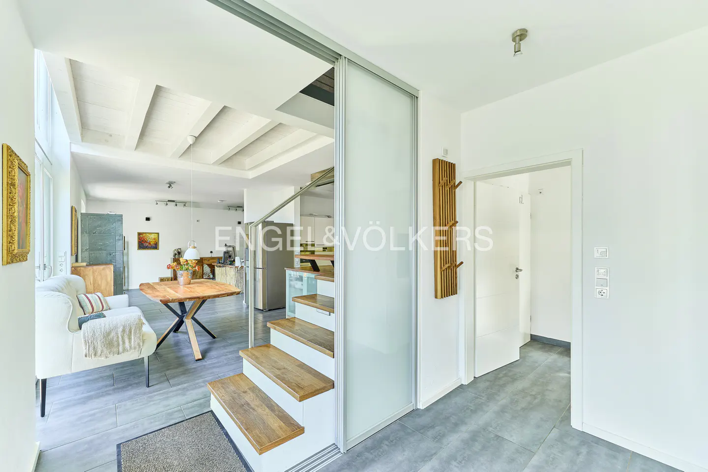 Interior view of a modern home with stairs, a table, and a white sofa. The walls are white, and the floor is gray.
