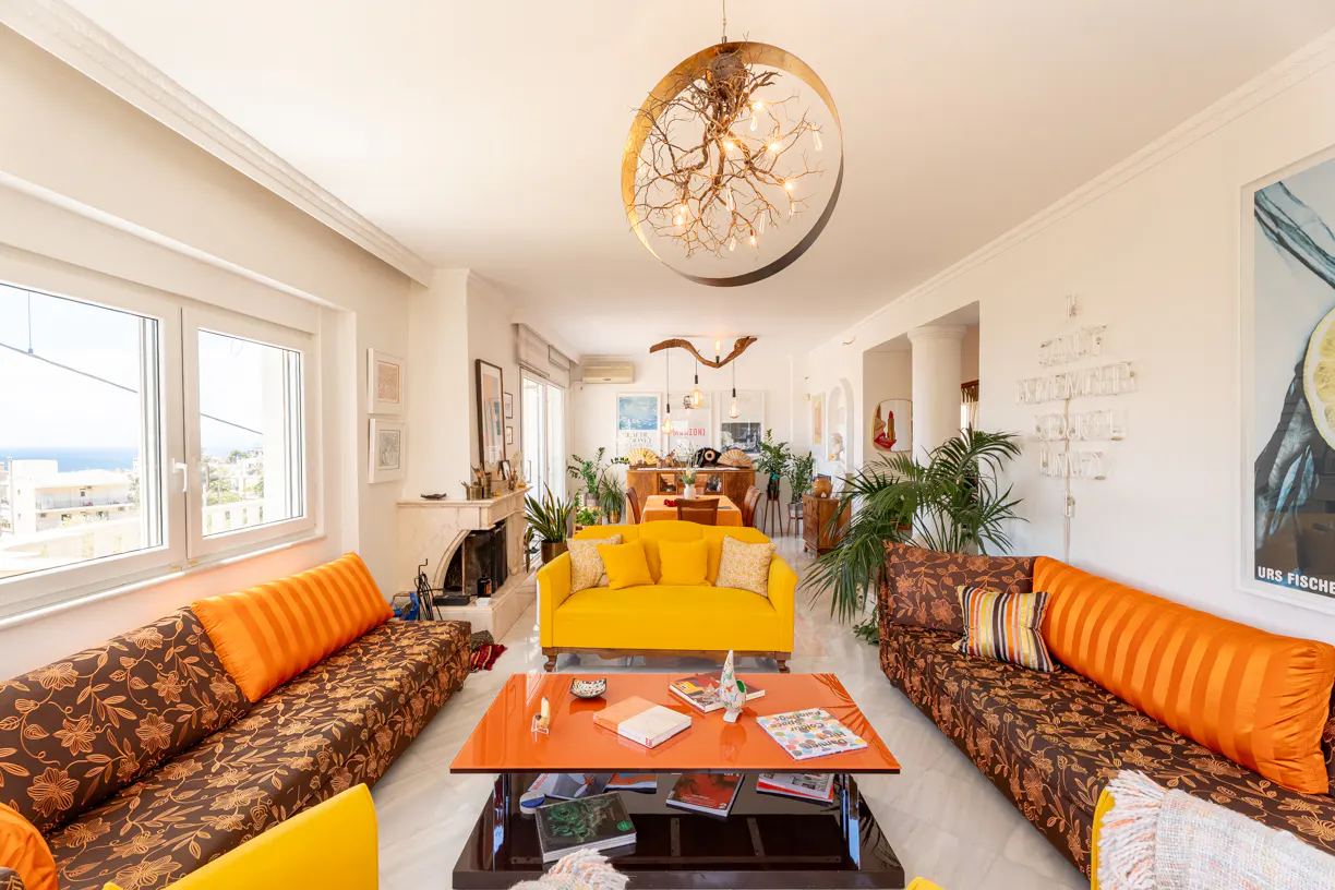 Bright living room with floral sofas, a yellow couch, orange coffee table, and a unique circular chandelier.