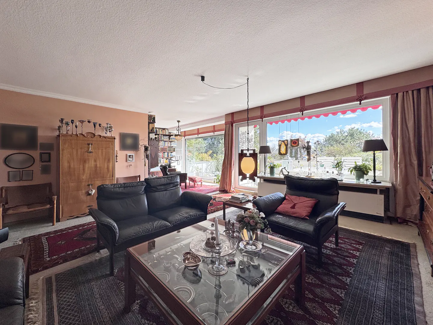 A living room with black leather sofas, a glass coffee table, and a large window with red curtains.