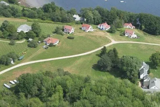 Aerial view of a green, grassy landscape with scattered houses with red roofs and a winding road near a body of water.