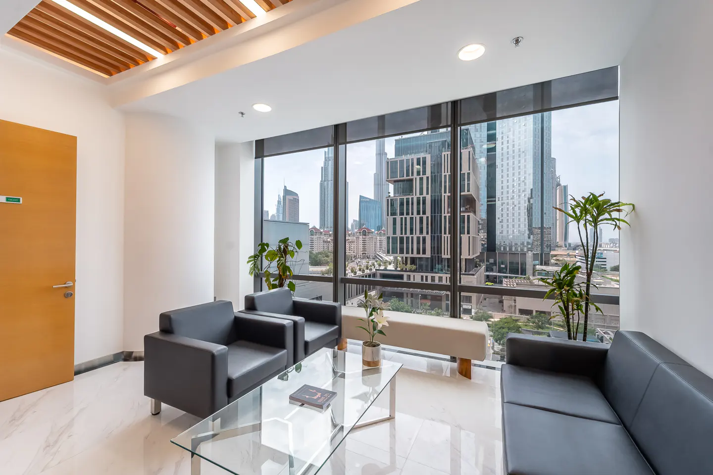 Bright office waiting area with black sofas, glass table, and a large window overlooking a city skyline.